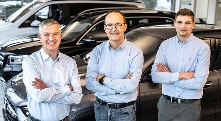 Drei Verkäufer stehen im Showroom vor Mercedes-Benz Modellen.
