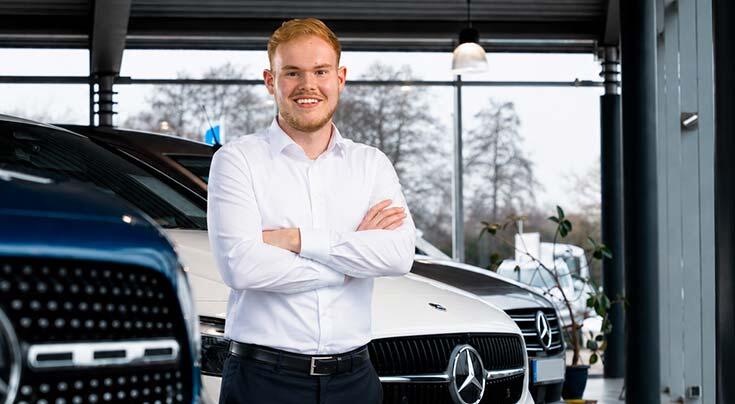 Verkäufer steht im Showroom vor Mercedes-Benz Fahrzeugen
