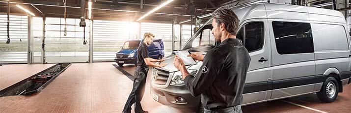 Zwei Mechaniker stehem in der Werksatt vor einem grauen Mercedes-Benz Transporter, im Hintergrund ein weiterer blauer Transporter