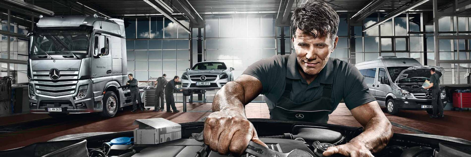Mechaniker bei Wartungsarbeiten an einem Fahrzeug in einer Mercedes-Benz Werkstatt mit Pkw, Transporter und Lkw.