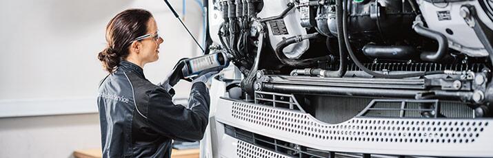 Mechatronikerin mit Werkzueg vor einem Mercedes-Benz Truck mit geöffneter Motorhaube.