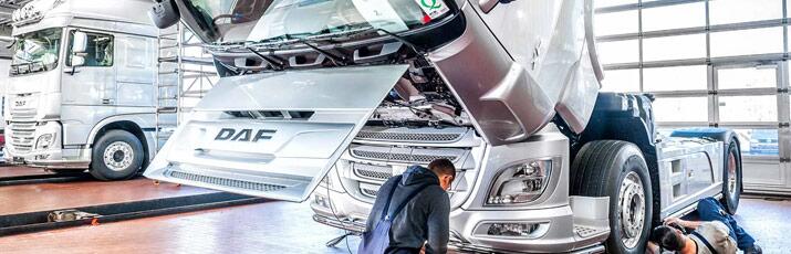 Zwei Mechatroniker reparieren ein DAF-Lkw in der Werkstatthalle, im Hintergrund eine zweiter DAF-Lkw.