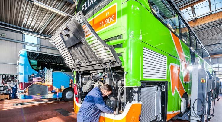 Mechaniker bei Wartungsarbeiten am geöffneten Motorraum eines grünen Reisebusses in einer Werkstatt.