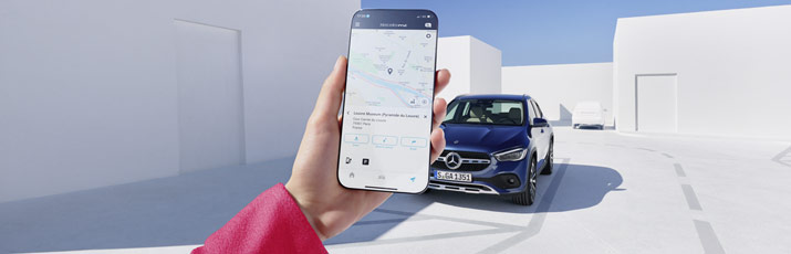 Im Vordergrund eine Fraeunhand mir ein Smartphone, im Hintergrund ein blauer Mercedes-Benz Pkw.